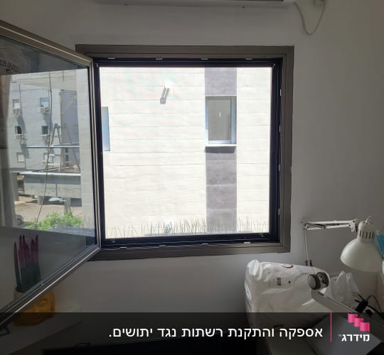 חלון אלומיניום עם פתיחה על ציר ורשת מותקנת בחדר
